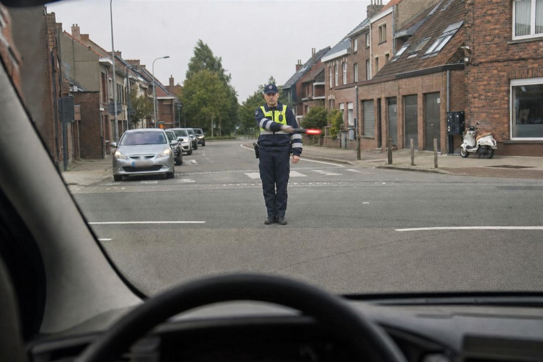 Agent belge tenant un feu rouge balancé transversalement, vu à travers le pare-brise